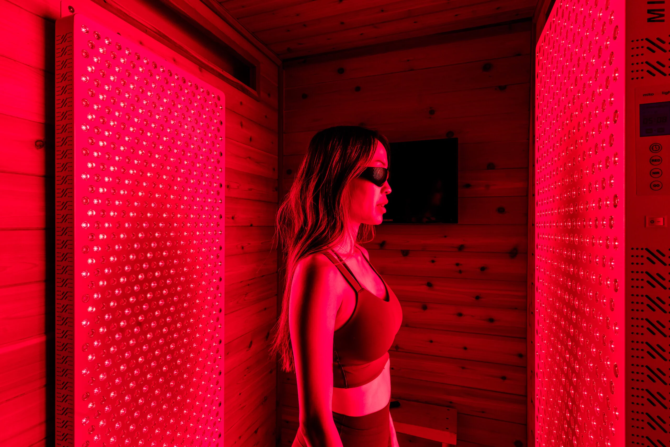 woman standing in a red-light panel therapy cabin